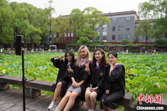 6月19日，时值一年毕业季，四川大学望江校区荷花池里的荷花盛开，成为了毕业生们的打卡圣地，吸引了众多毕业生拍照留念。图为毕业生在荷花池边拍照留念。中新社记者 安源 摄