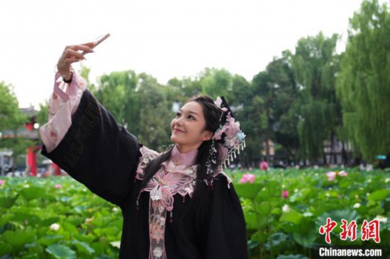 6月19日，时值一年毕业季，四川大学望江校区荷花池里的荷花盛开，成为了毕业生们的打卡圣地，吸引了众多毕业生拍照留念。图为毕业生在荷花池边拍照留念。中新社记者 安源 摄